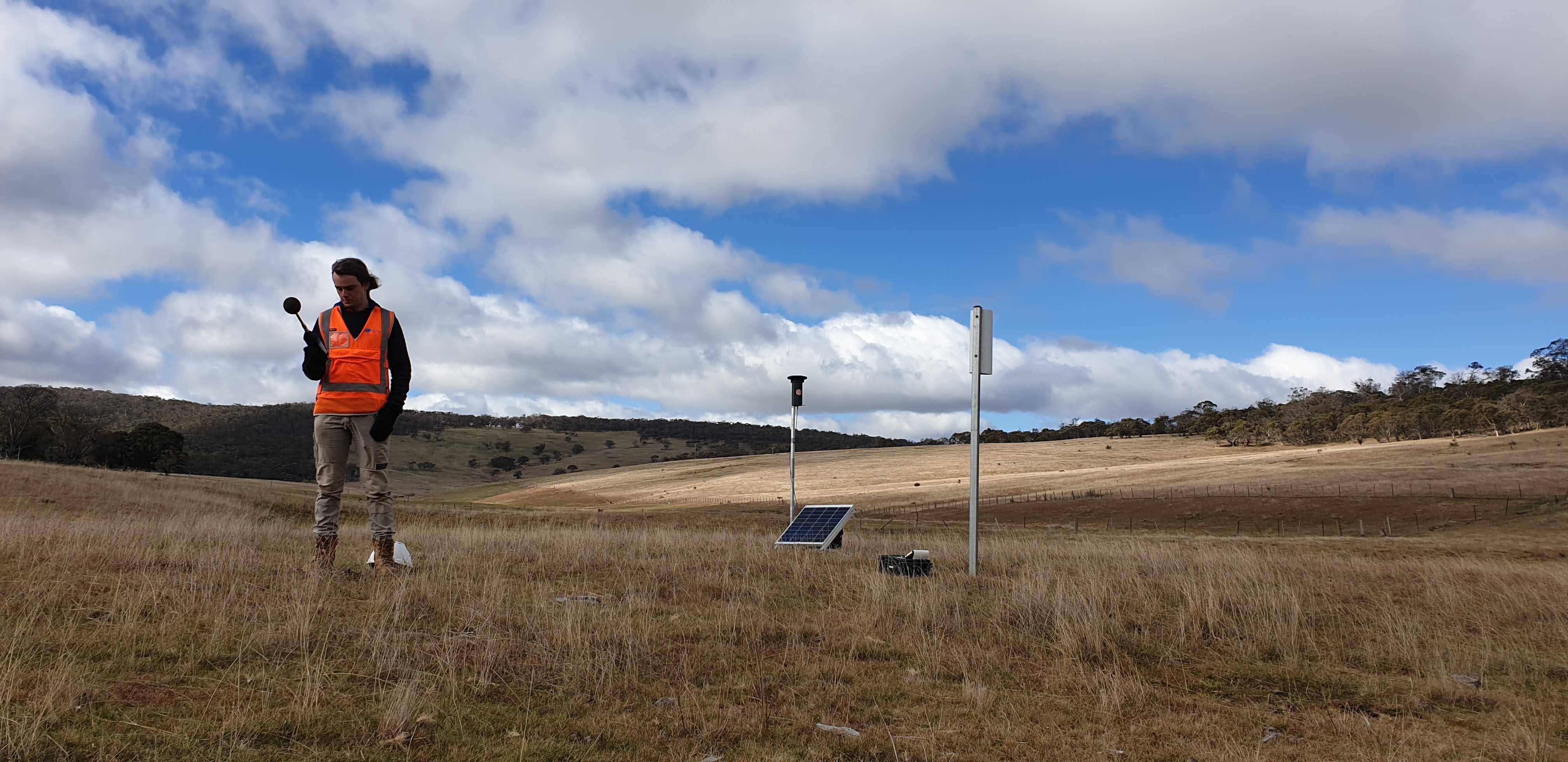 Acoustic consultant in high-vis vest undertaking attended noise monitoring with a Type 1 sound level meter next to a SiteHive Hexanode Noise and Air Quality Monitor and a dust deposition gauge in the Snowy Mountains for the Snowy Hydro 2.0 Project